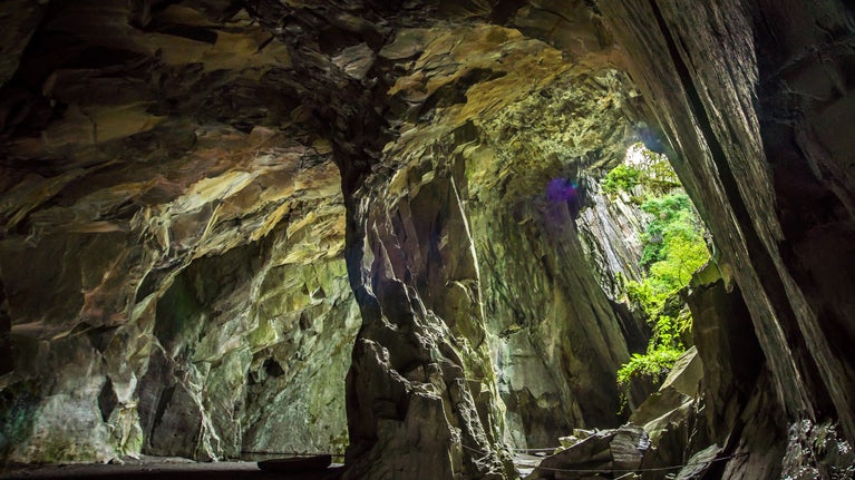 A huge cavern supported by one large rock pillar with a cave opening, Cathedral Quarry, Cumbria